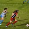two women playing soccer on field