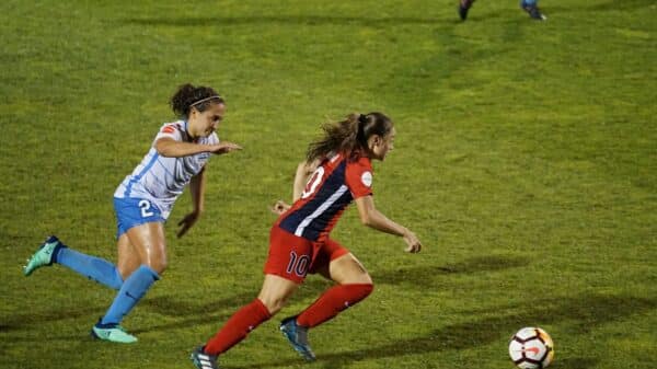 two women playing soccer on field