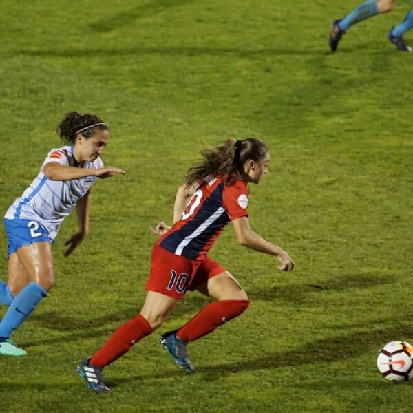 two women playing soccer on field