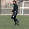 Male soccer coach in black sportswear practicing on a grass field.