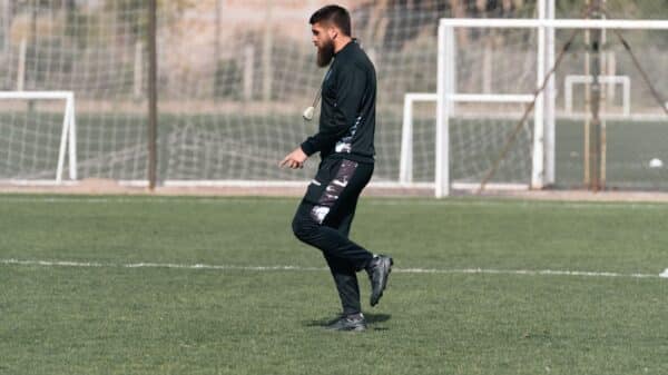 Male soccer coach in black sportswear practicing on a grass field.